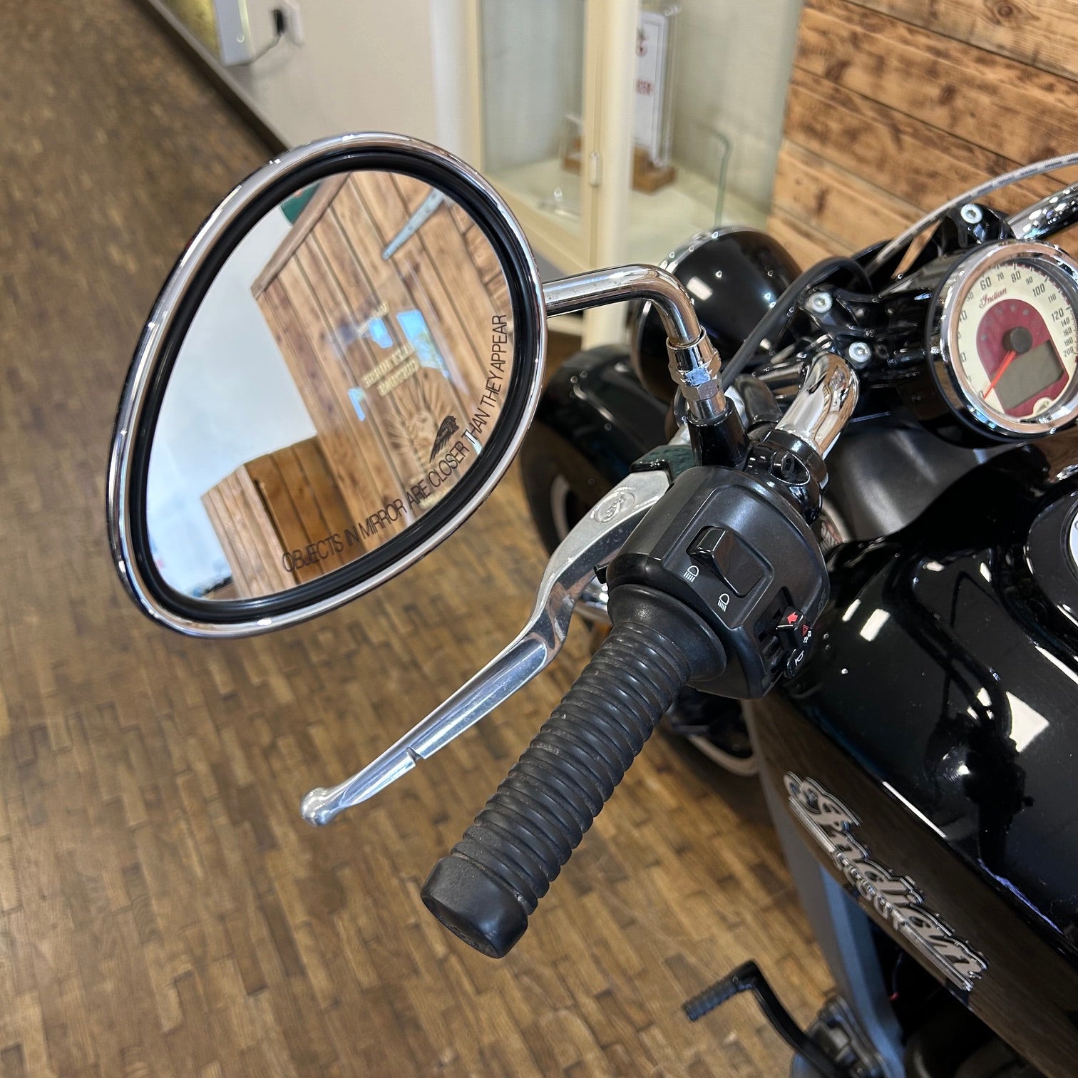 Close-up of a motorcycle handlebar with mirror and dashboard, indoors.
