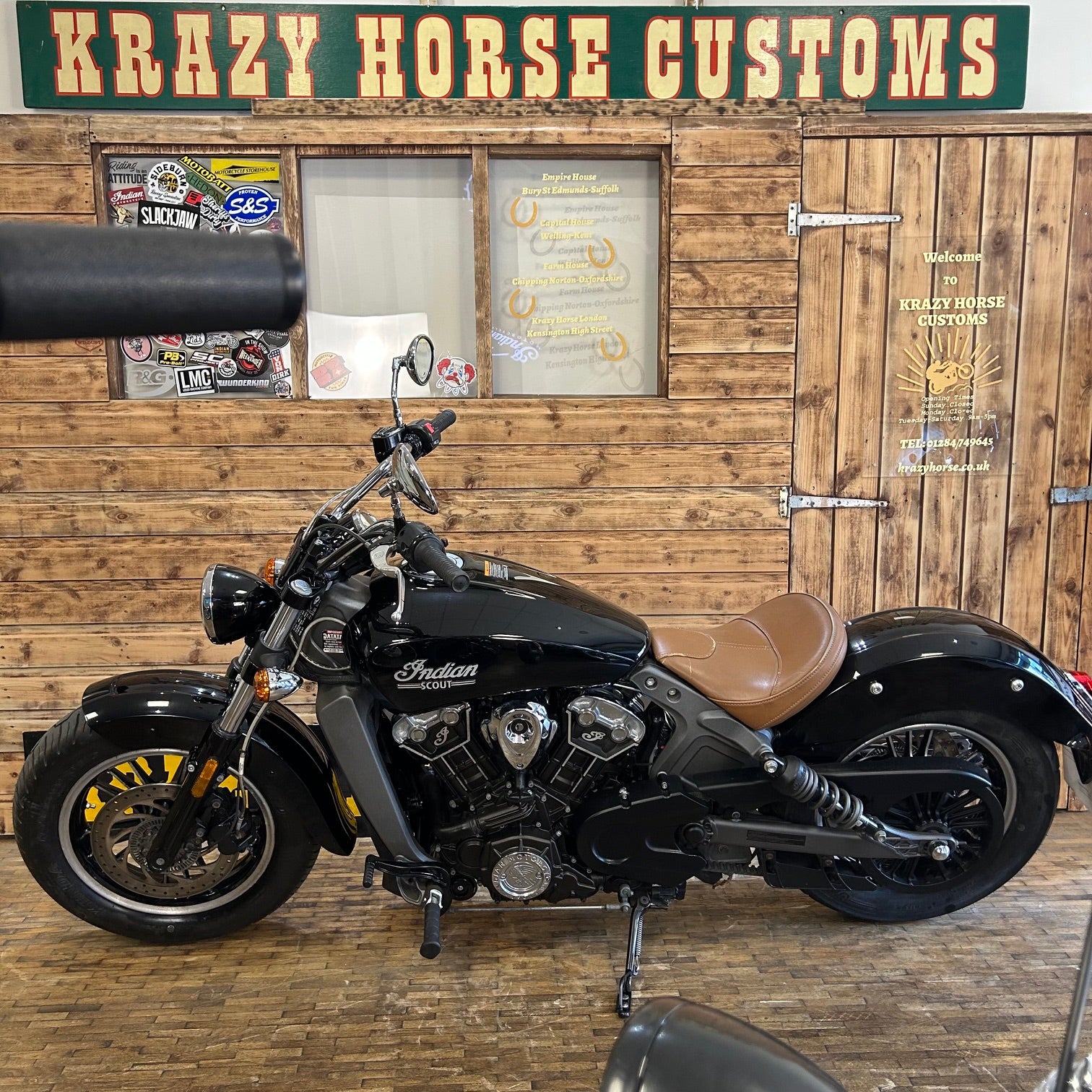 Black Indian motorcycle in front of a wooden wall with 'Krazy Horse Customs' sign.