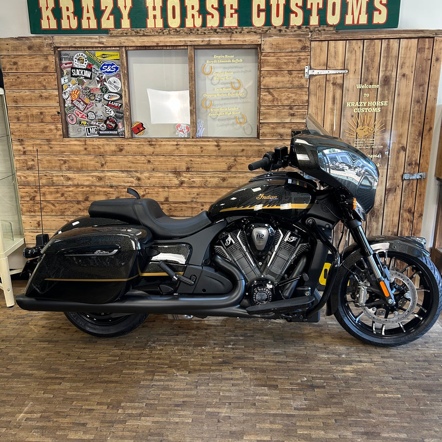 Black motorcycle parked inside a building with wooden walls and a sign reading 'Krazy Horse Customs'.
