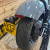 Close-up of a motorcycle's rear wheel and license plate against a wooden wall.
