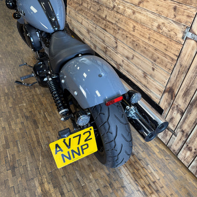 Gray motorcycle with a yellow license plate on a wooden floor.