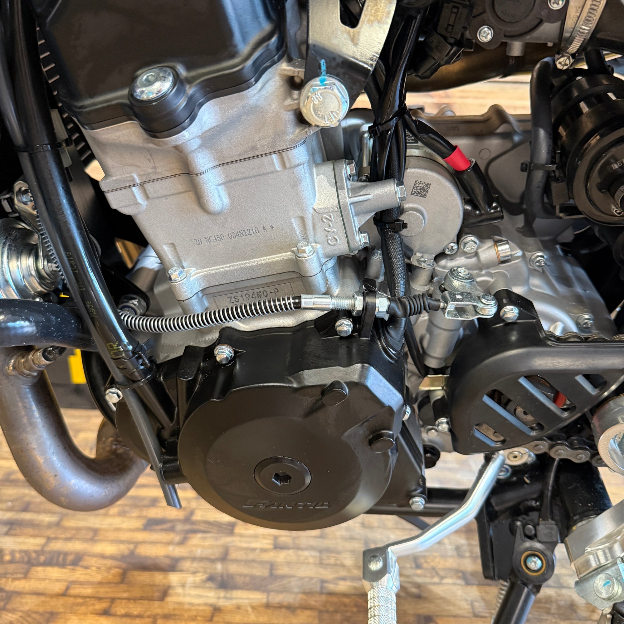 Close-up of a motorcycle engine and mechanical components on a wooden floor.