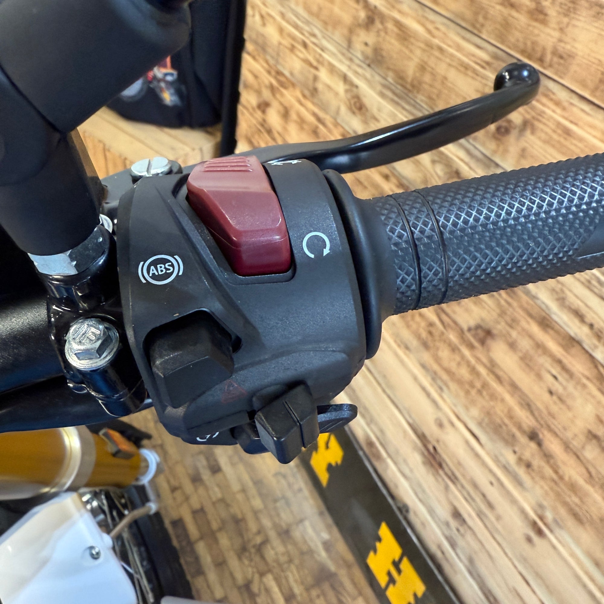Close-up of a motorcycle handlebar with ABS and brake lever on a wooden floor.