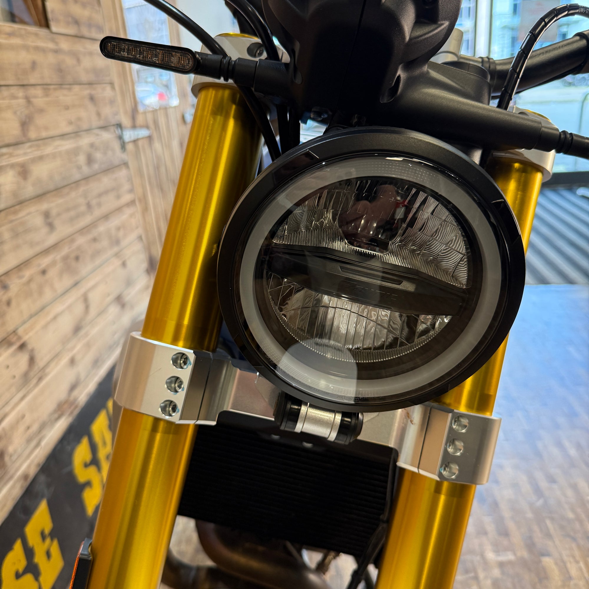 Close-up of a motorcycle headlight with gold forks and blurred background