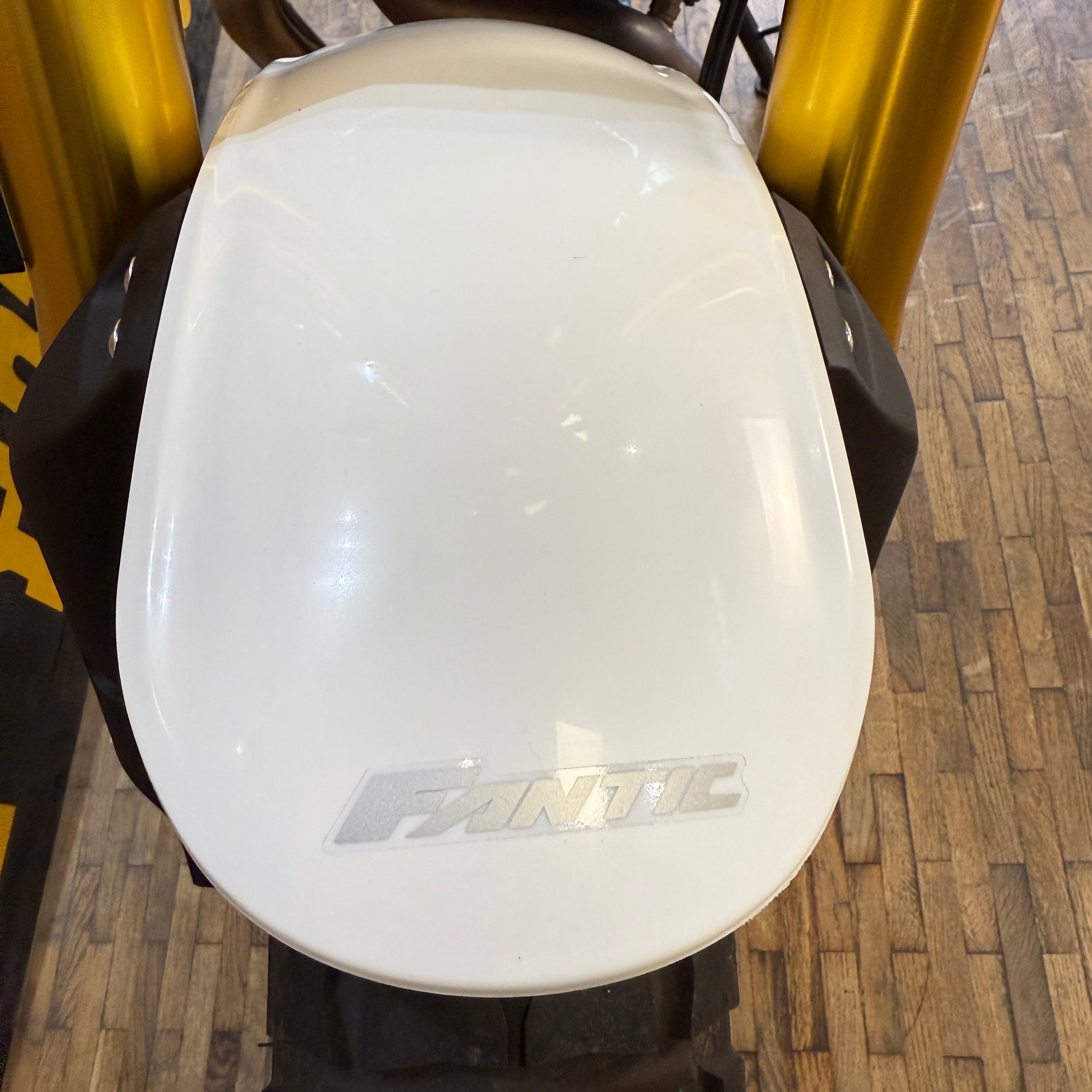 White motorcycle seat with 'Fantic' branding on a wooden floor.
