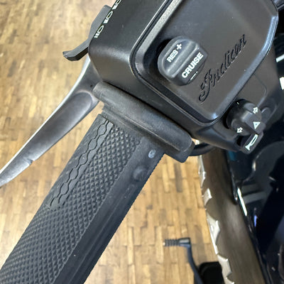 Close-up of a motorcycle handlebar with 'Indian' branding on a wooden floor background
