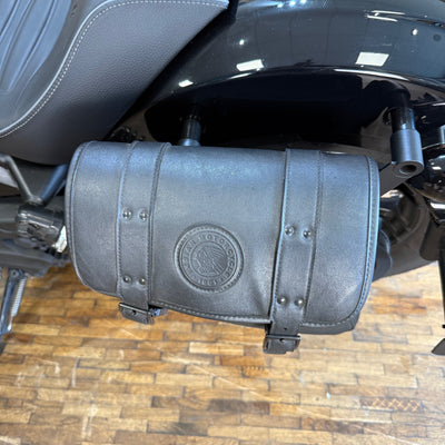 Black leather motorcycle saddlebag with brand logo on a wooden floor