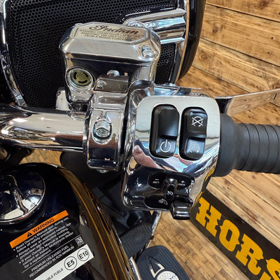 Close-up of a motorcycle handlebar with control switches on a wooden floor.