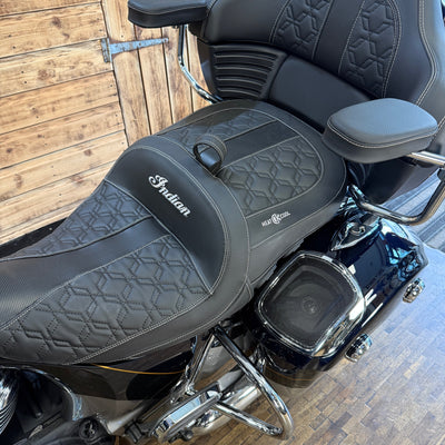 Close-up of a motorcycle seat with 'Indian' branding on a wooden floor.