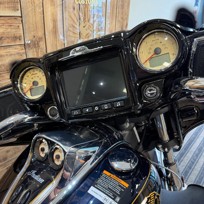 Close-up of a motorcycle dashboard with an 'Indian' logo, featuring two round gauges and a screen.