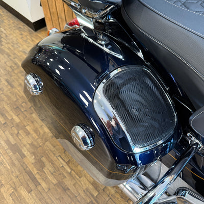 Close-up of a motorcycle seat with a speaker enclosure on a wooden floor.