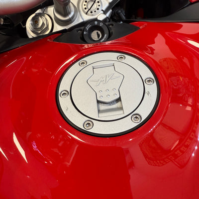 Close-up of a red motorcycle fuel tank with a silver cap featuring branding.