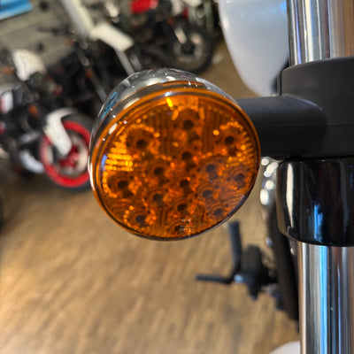 Close-up of a motorcycle turn signal with a blurred background of other motorcycles.