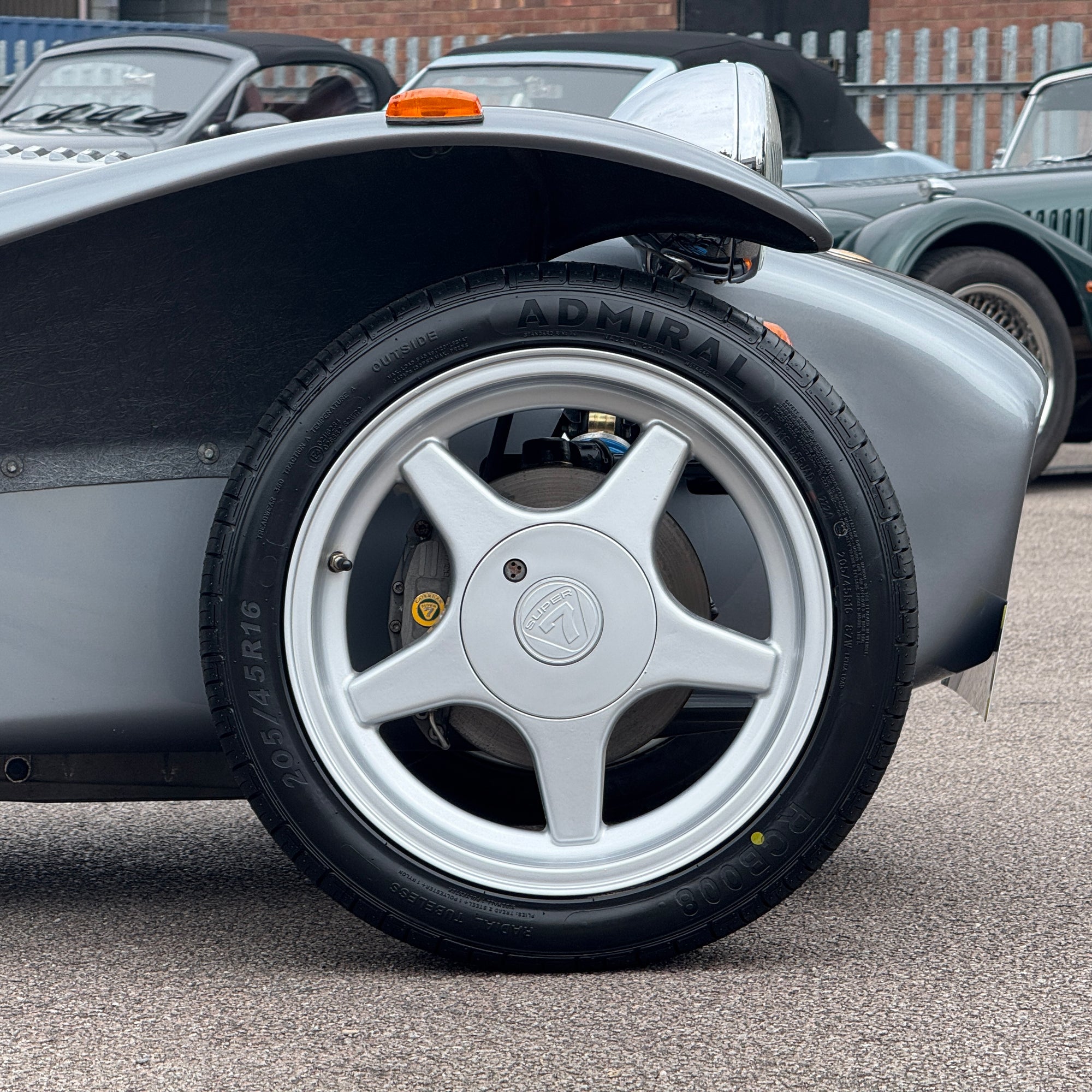 Close-up of a car wheel with a visible brand logo on a road.