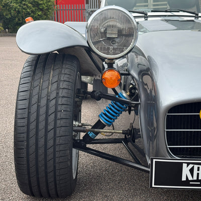 Close-up of a classic car's front wheel and suspension system on a road.