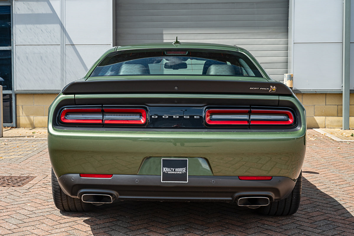 Green Dodge car with red taillights parked on a brick driveway.
