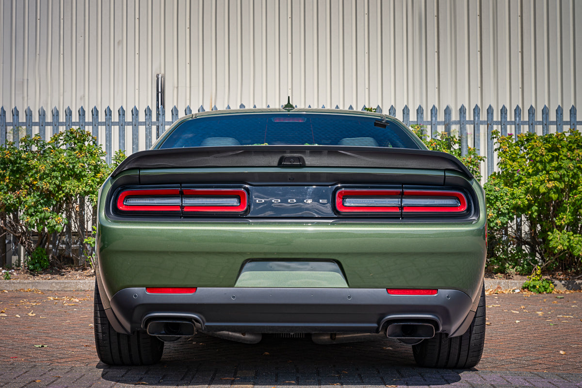 Green Dodge car with red taillights parked in front of a white building.
