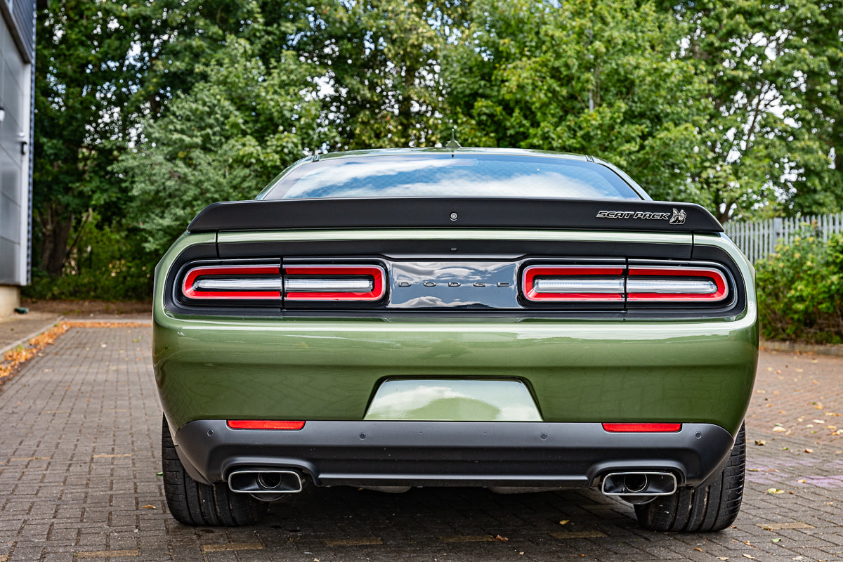 Green car with black roof and red taillights parked on a paved surface with trees in the background