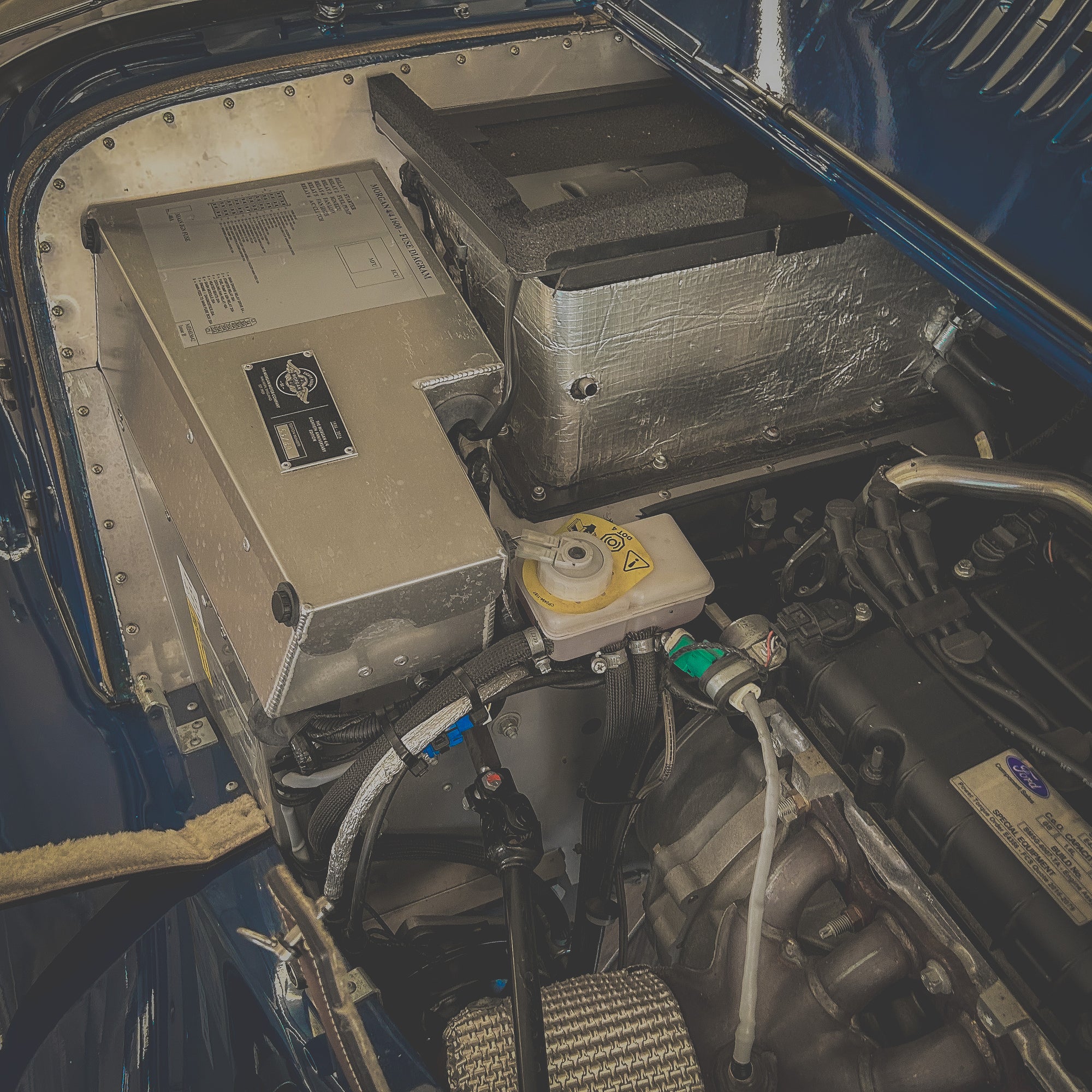 Close-up of vehicle engine compartment with battery and electrical components.