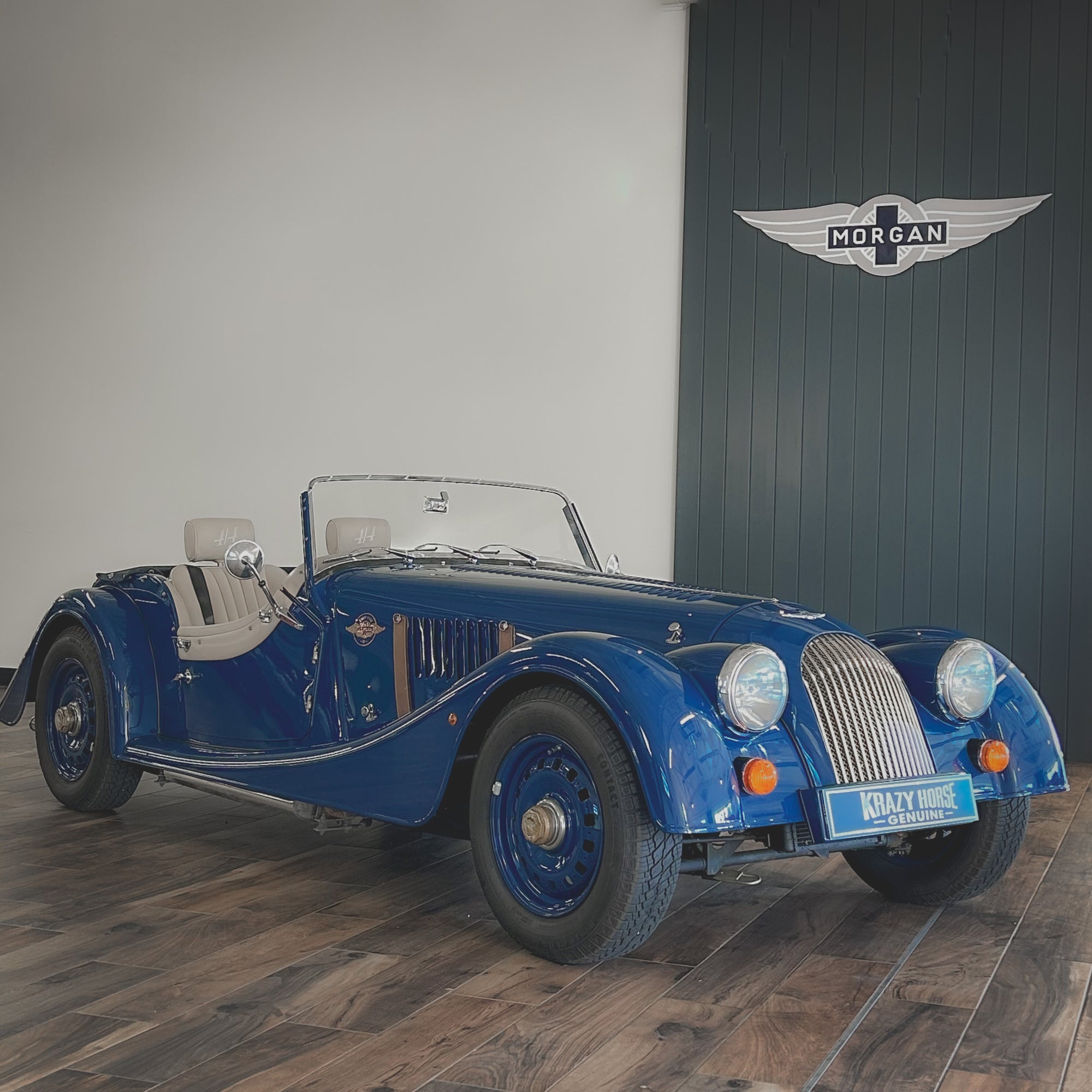 Blue vintage car in a showroom with a visible brand logo on the wall.