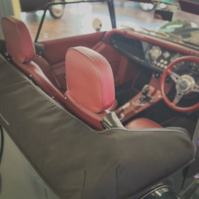 A close-up view of a car interior featuring red leather seats and a matching red steering wheel, with a dark gray fabric cover draped over the front seat area.