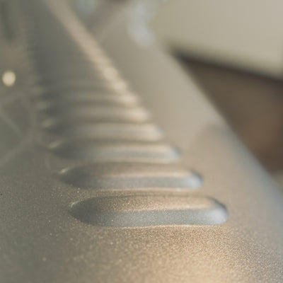 Close-up of a metallic silver textured surface with a series of parallel horizontal grooves, shown in soft focus with a shallow depth of field.