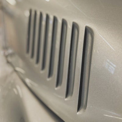 Close-up of a metallic silver car body with vertical vent slits and a glossy finish.