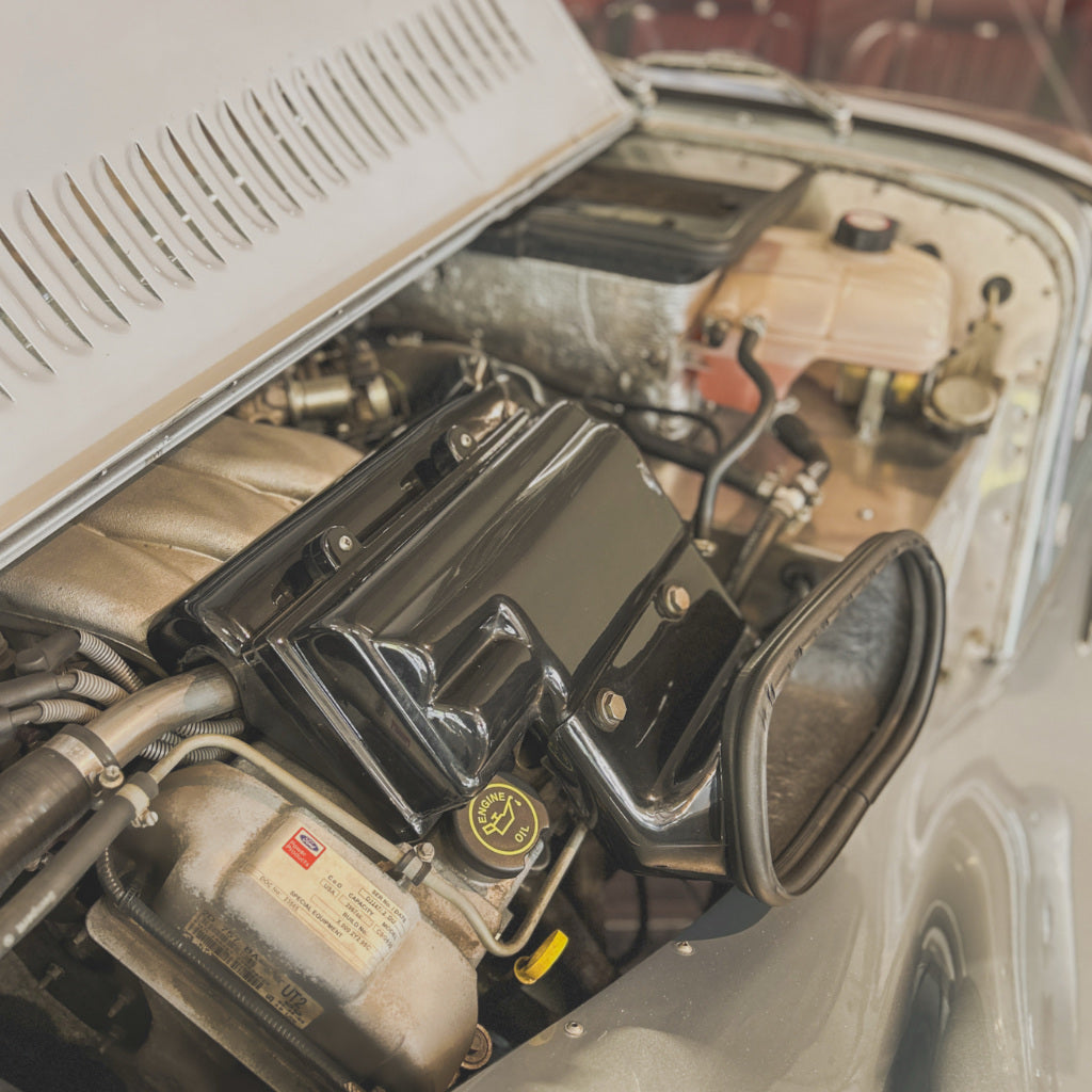 A close-up view of a car engine bay with a glossy black air filter housing and matching black gasket attached to a silver vehicle.