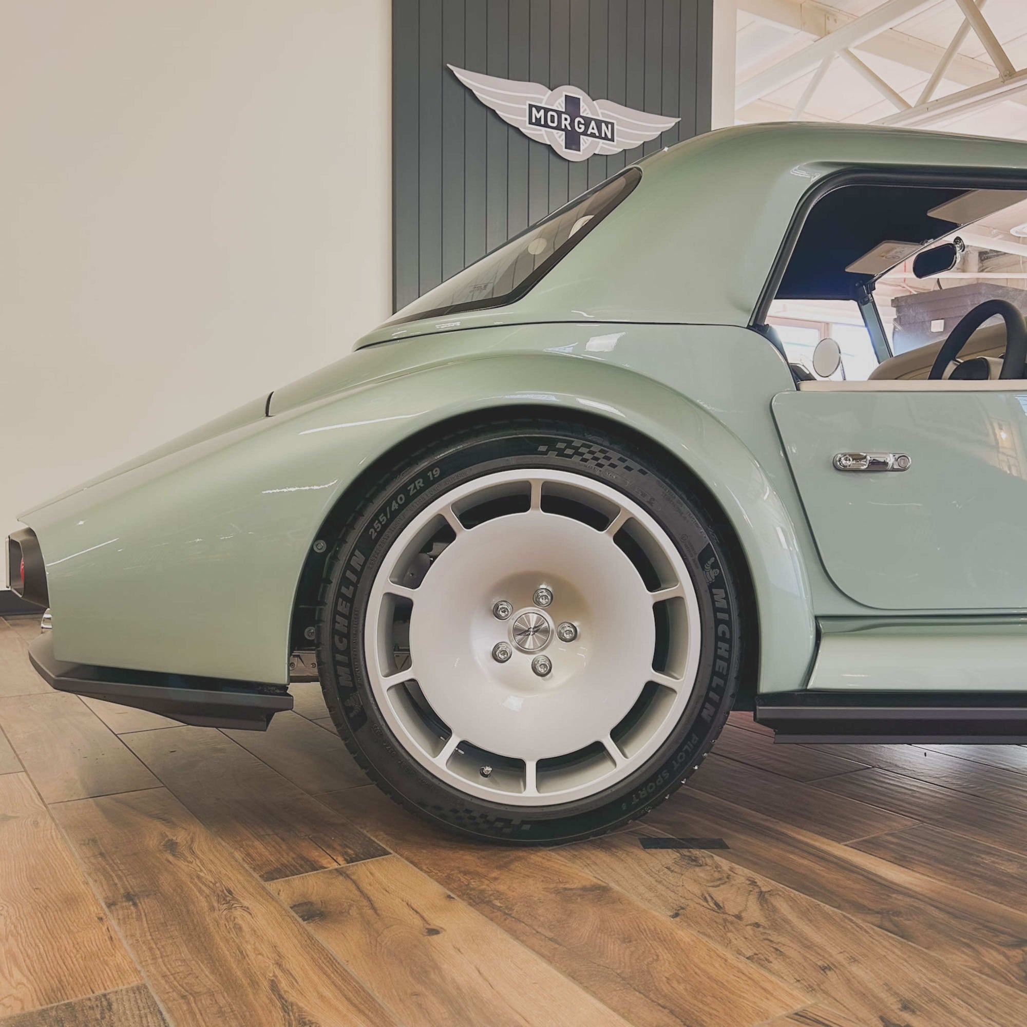 Light green sports car with white wheels on a wooden floor, brand logo in the background