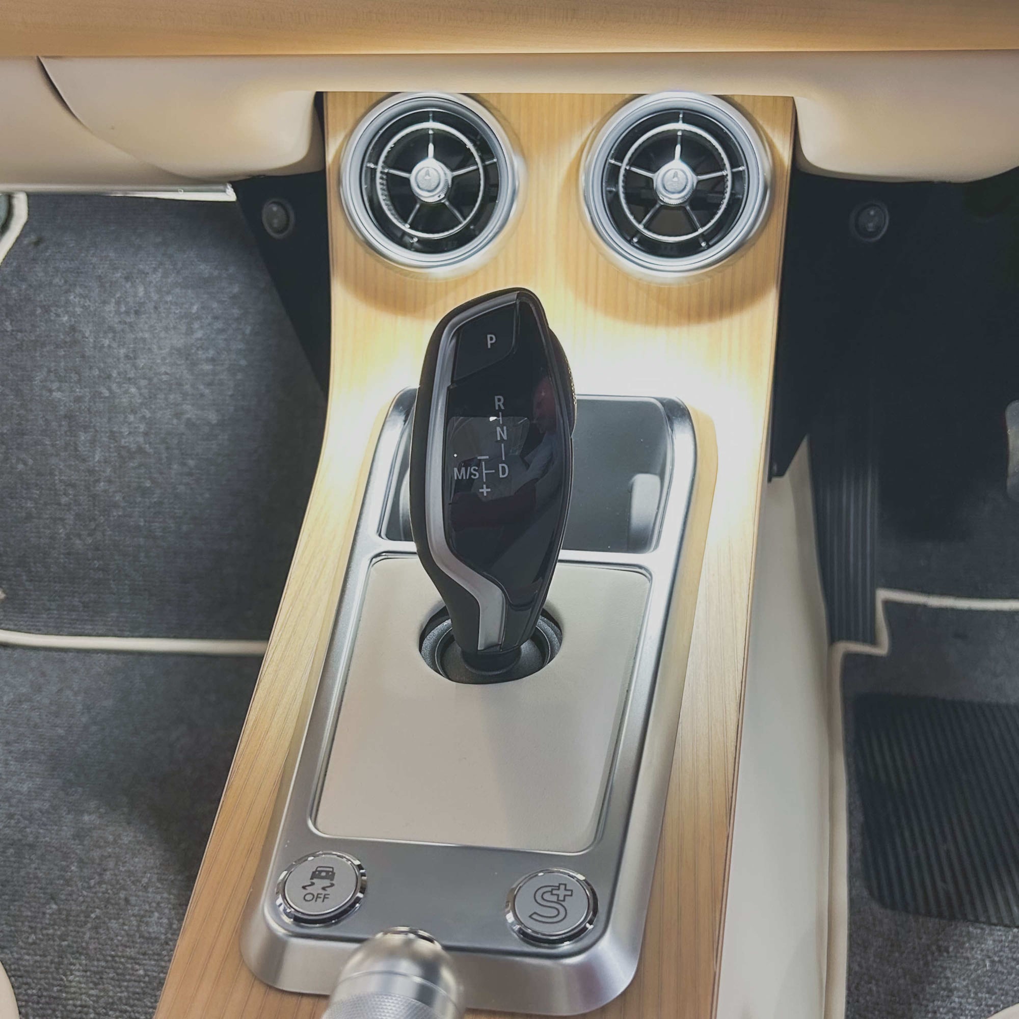 Car gear shift lever with wooden panel and air vents in a vehicle interior.