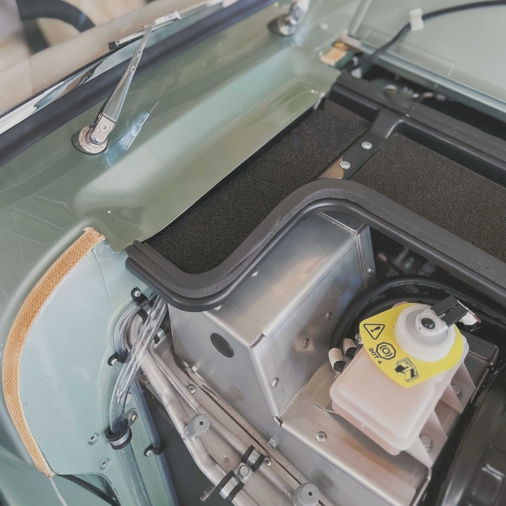 Close-up of a vehicle's open hood with mechanical components and a yellow warning label.