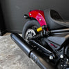 Close-up of a motorcycle with a red fuel tank and black exhaust on a concrete floor.
