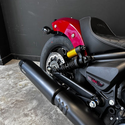 Close-up of a motorcycle with a red fuel tank and black exhaust on a concrete floor.