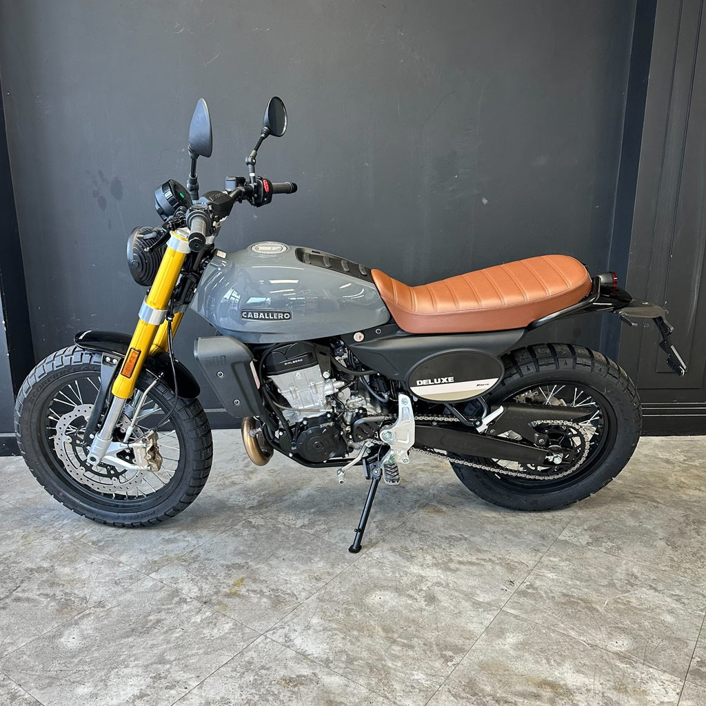 Motorcycle with a brown seat and yellow fender on a gray floor against a black wall.