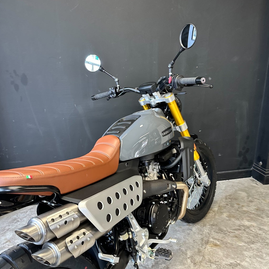 Motorcycle with brown seat and silver exhaust against a dark wall