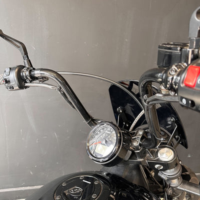 Close-up of a motorcycle handlebar with headlight and controls against a gray background