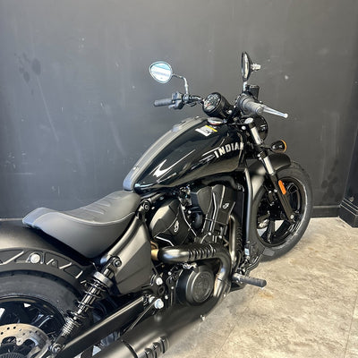 A black Indian motorcycle with matte and gloss black finishes, parked indoors against a dark gray wall on a light gray concrete floor.