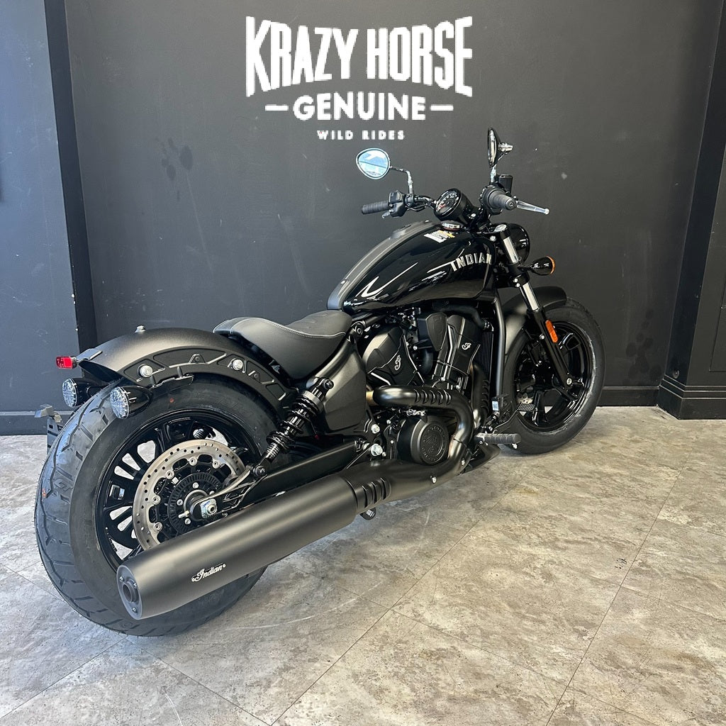 A black Harley-Davidson motorcycle with a matte finish is parked indoors against a dark gray wall with 'Krazy Horse Genuine Wild Riders' branding. The showroom floor is gray tile.