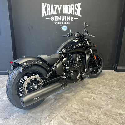 A black Harley-Davidson motorcycle with a matte finish is parked indoors against a dark gray wall with 'Krazy Horse Genuine Wild Riders' branding. The showroom floor is gray tile.