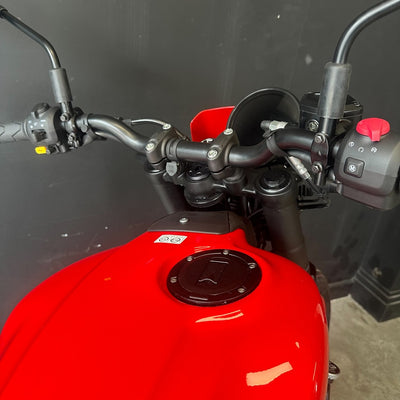 Close-up of a red motorcycle tank and black handlebars against a dark gray background.