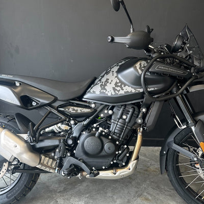 A Royal Enfield motorcycle with a matte black and gray camouflage pattern on the fuel tank and side panels, photographed indoors against a dark gray wall.