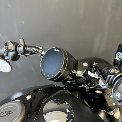 Close-up of a motorcycle dashboard with a round digital display and chrome handlebars, mounted on a black bike body against a gray background.