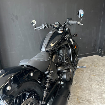 A black cruiser motorcycle with gold accents, photographed indoors against a dark gray wall and light gray concrete floor.