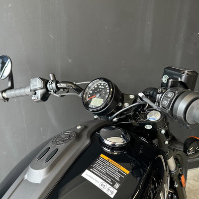 Close-up of a black motorcycle dashboard, handlebars, and fuel tank against a dark gray background.