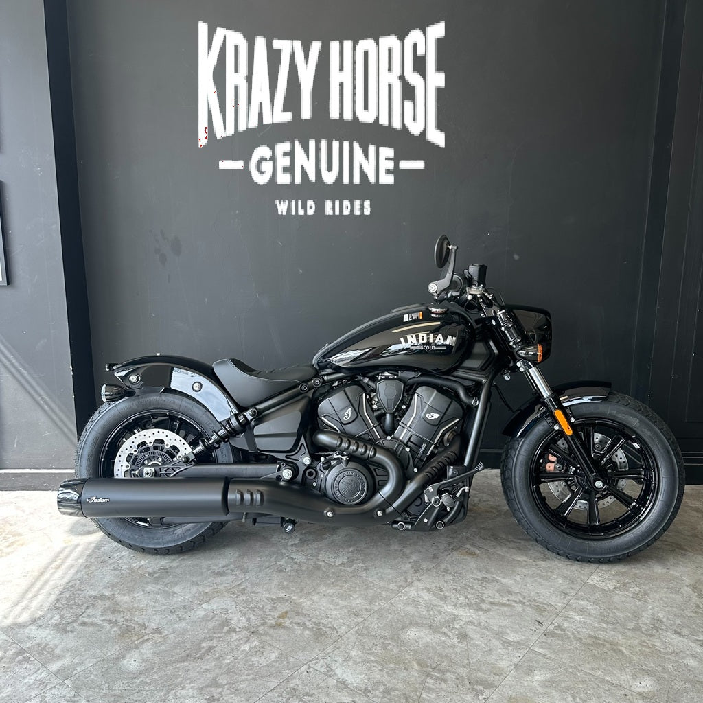 A black Indian Harley-Davidson Softail motorcycle is parked indoors against a dark gray wall with large white 'Krazy Horse Genuine' branding and the smaller text 'Wild Rides' below it.