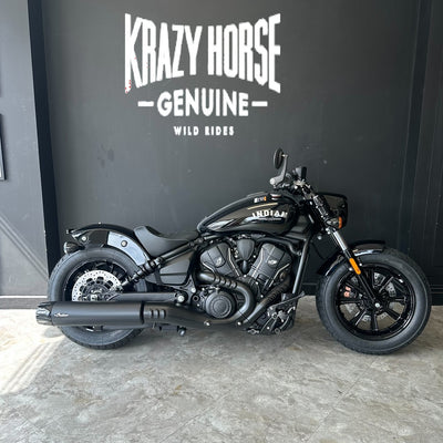 A black Indian Harley-Davidson Softail motorcycle is parked indoors against a dark gray wall with large white 'Krazy Horse Genuine' branding and the smaller text 'Wild Rides' below it.