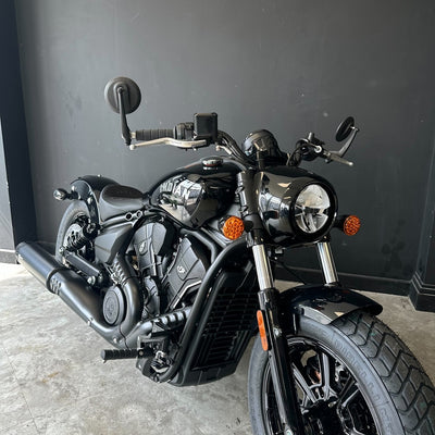 A black cruiser motorcycle photographed indoors against a dark gray wall and concrete floor.