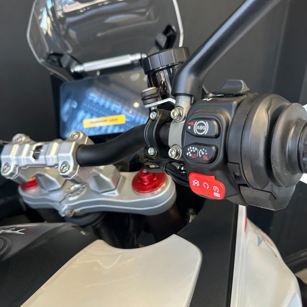 Close-up of a motorcycle handlebar area showing the right handlebar grip with controls, a red emergency stop button, silver fork hardware, and part of the white and black motorcycle body.