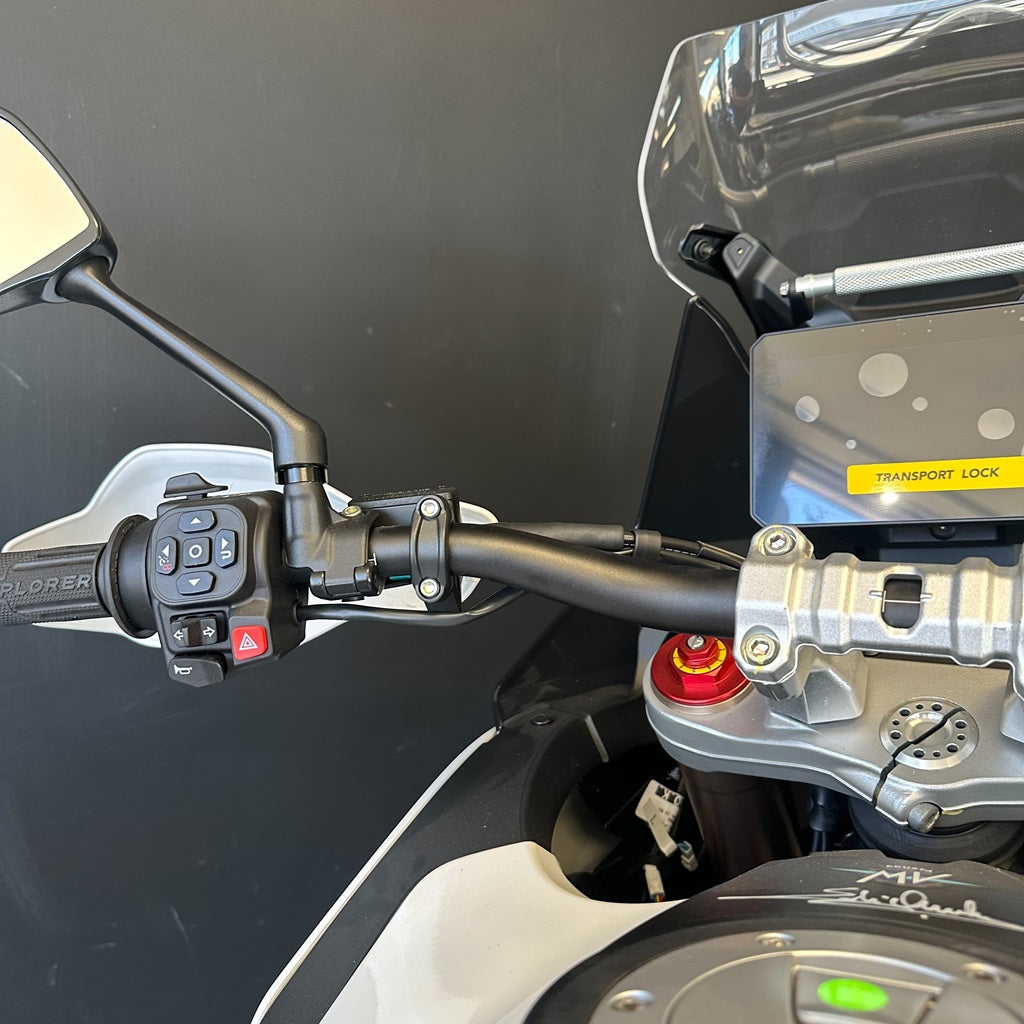Close-up of a motorcycle handlebar area showing the left handlebar grip with controls, a black windscreen, a silver engine block, and a yellow Transport Lock sticker.