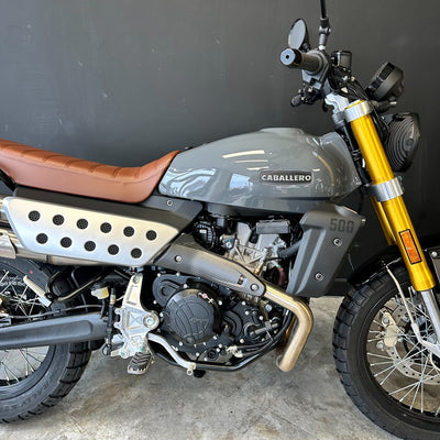 A gray and brown motorcycle with a gold front fork, photographed indoors against a dark gray wall and concrete floor. The tank shows the brand name CABALLERO and the number 500.